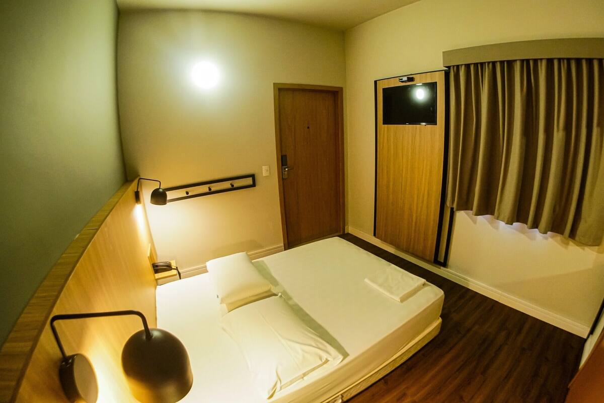 Une chambre d’hôtel avec un lit, une lampe de chevet, une porte et un rideau.