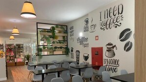 A modern cafe with tables and chairs, a wall with coffee-related decor, and a display of plants. - Hotel Graal Inn Uberaba (Uberaba)