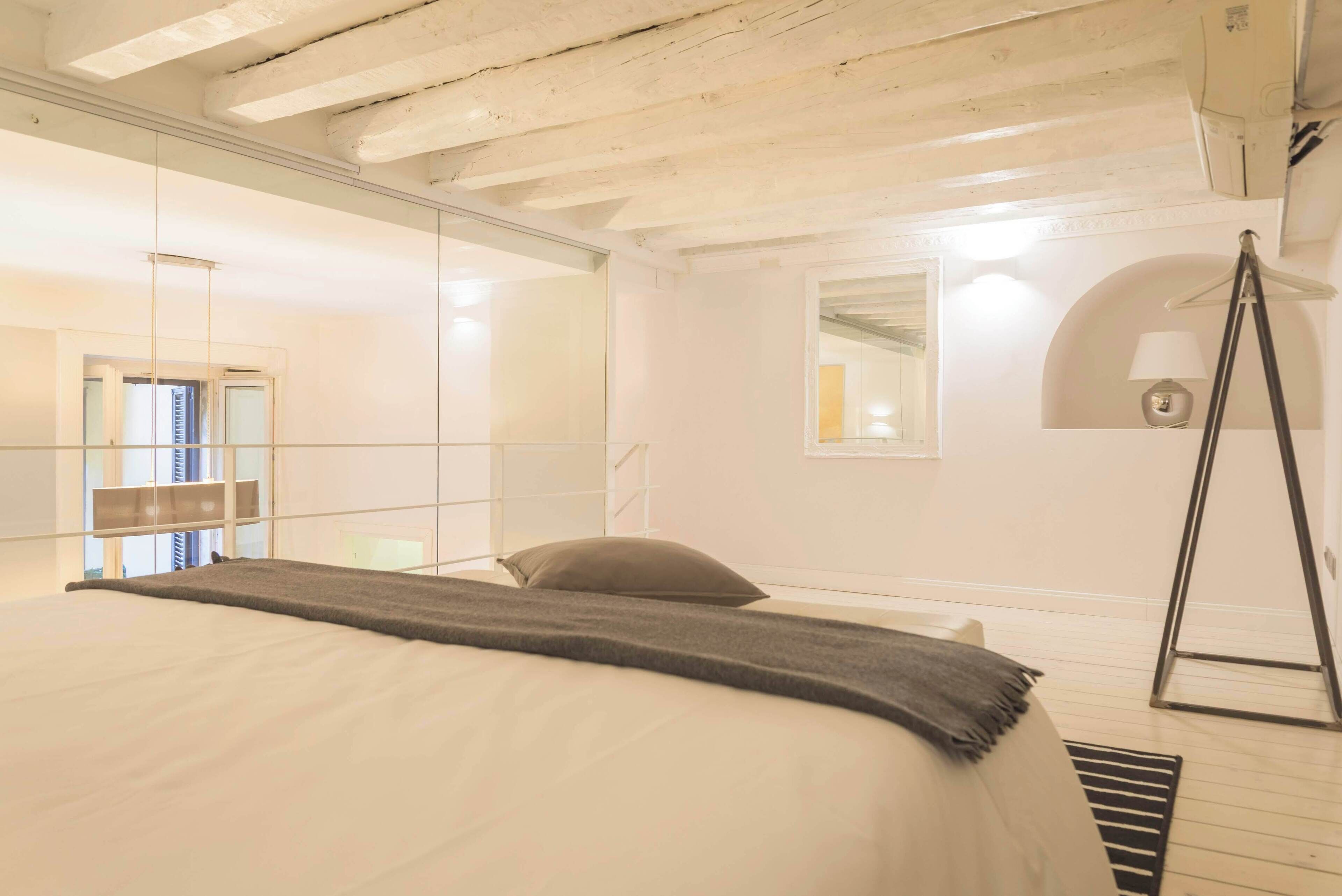 A bedroom with a bed, a hanging chair, a mirror, and a small lamp.