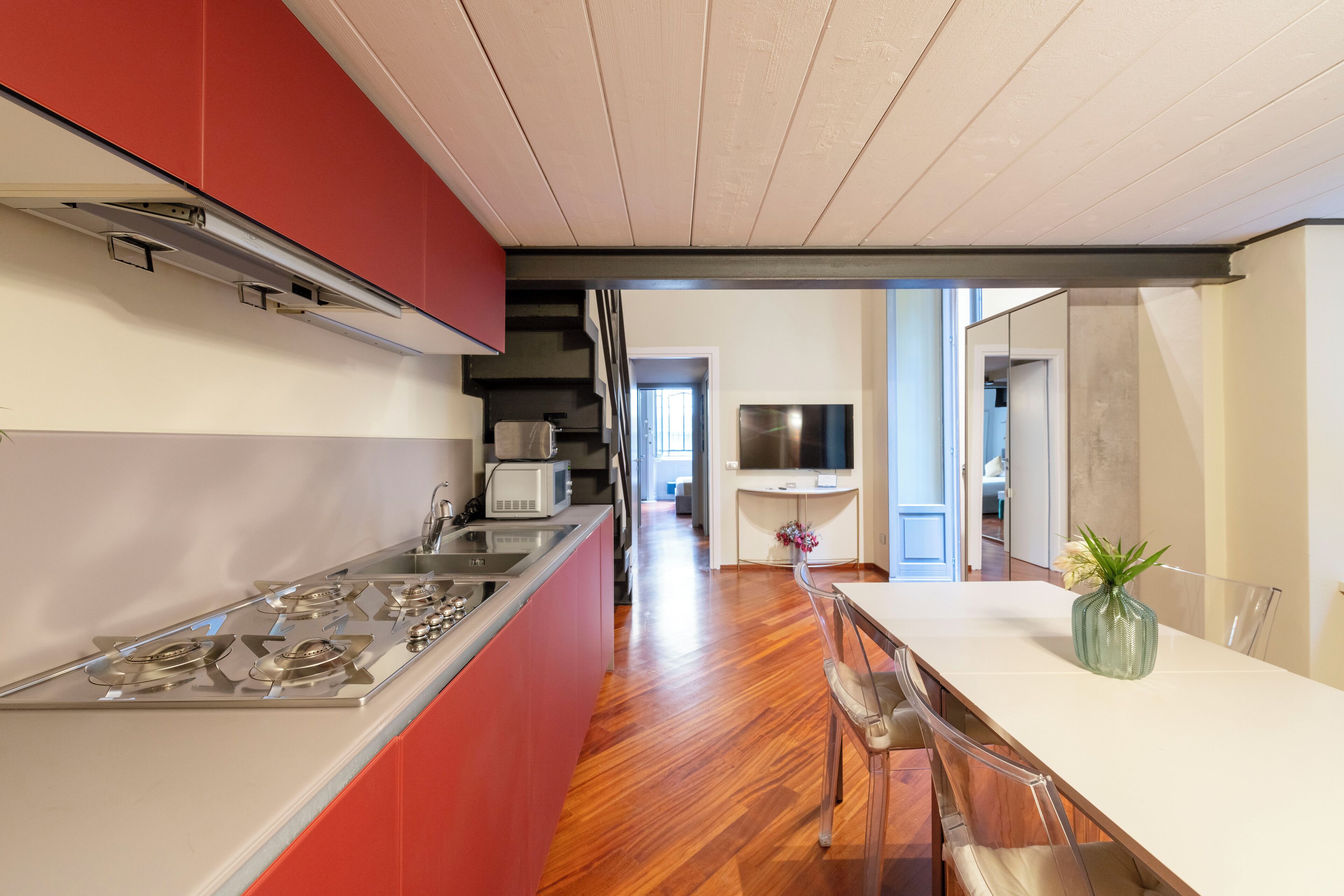 A modern kitchen with a central island, red cabinetry, and a dining area with a white table and chairs.