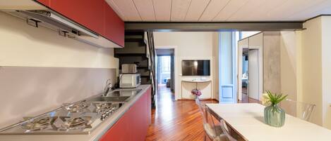 A modern kitchen with a central island, red cabinetry, and a dining area with a white table and chairs.