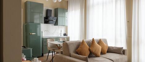 A modern living room with a sofa, a dining table, and a kitchen area with cabinets and a refrigerator.