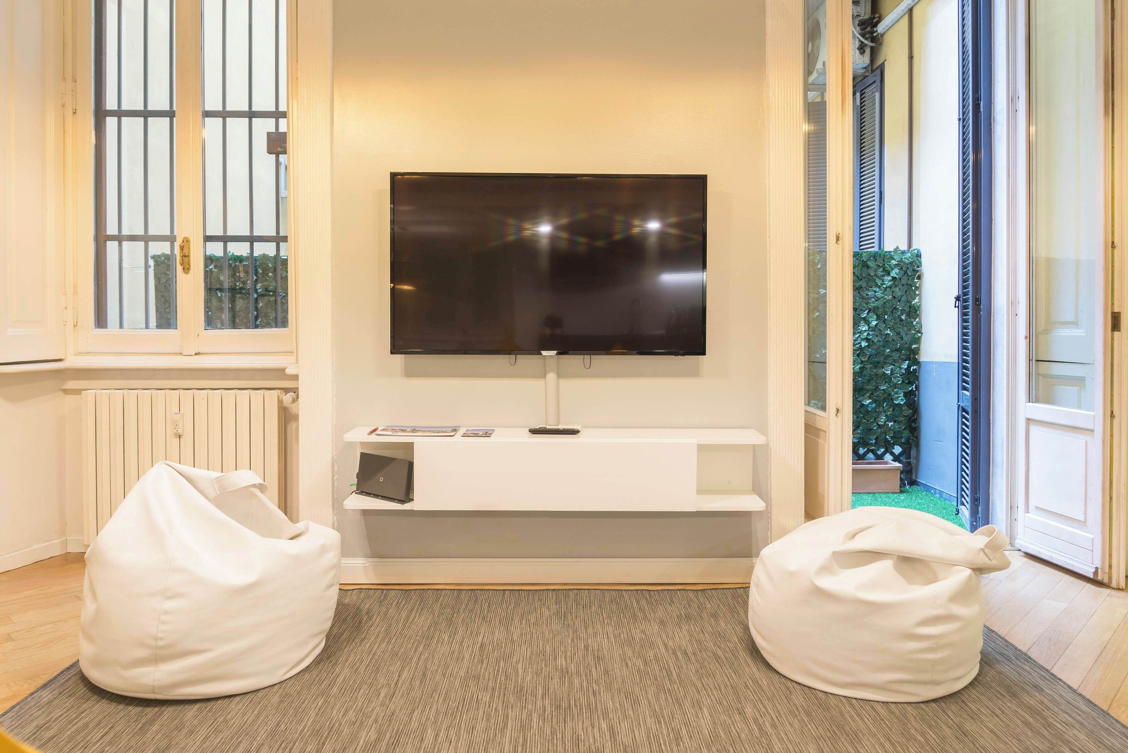 A living room with a flat-screen TV mounted on the wall, a white bench, and two white bean bags.