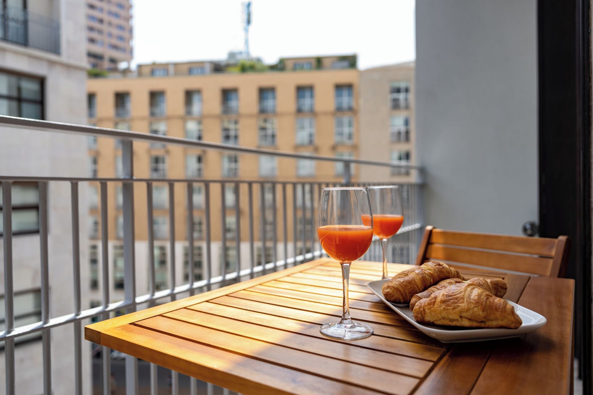 Uma varanda com uma mesa de madeira, dois copos de sumo de laranja e croissants.
