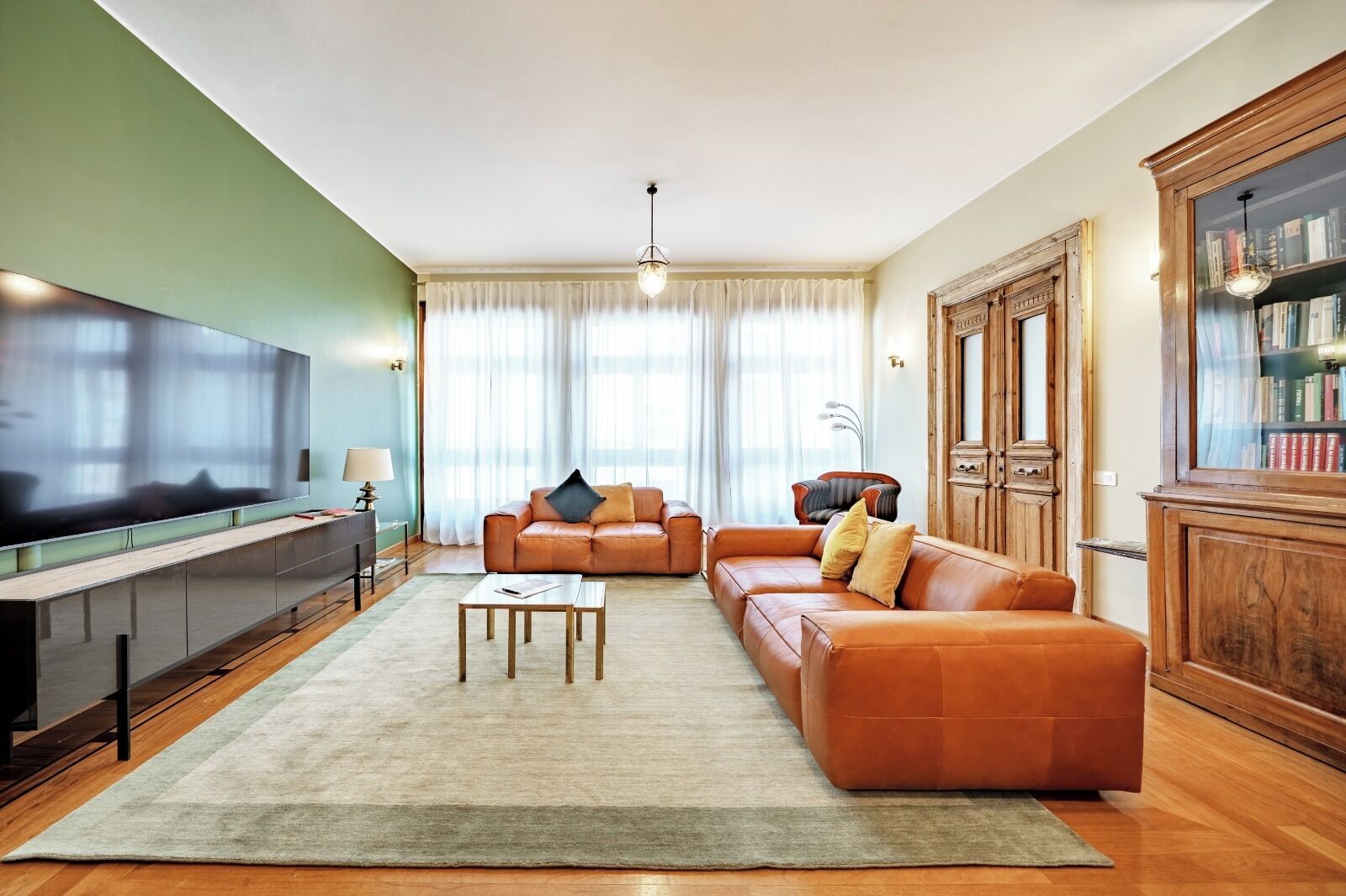 A living room with a large flat-screen TV, leather sofa, wooden cabinet, and a bookshelf.