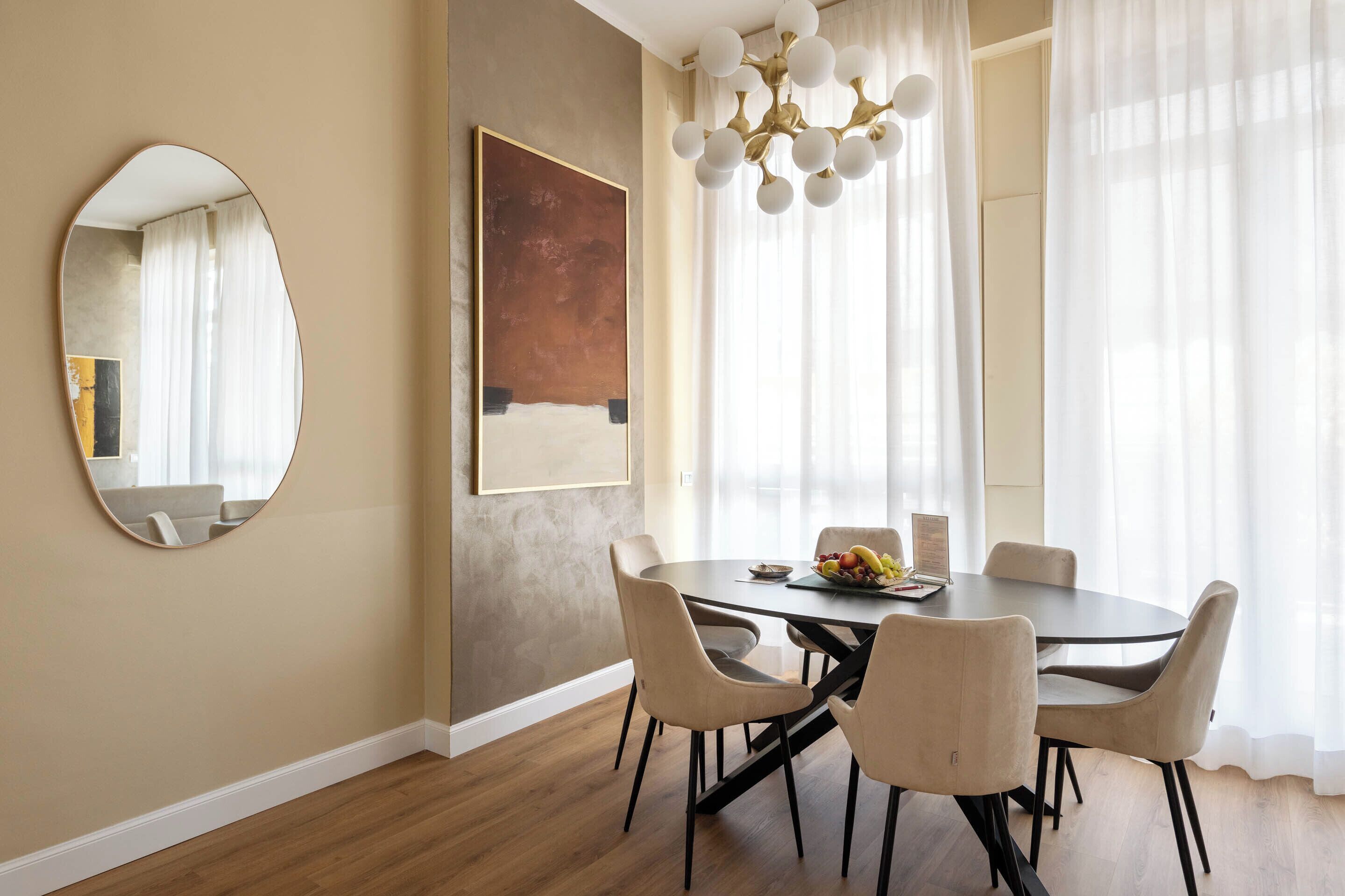 A dining area with a round table, six chairs, a chandelier, and artwork on the walls.