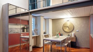 A modern kitchen with a dining area, wooden flooring, and a large wall clock. - Heart Milan Apartments Duomo Missori (Milan)