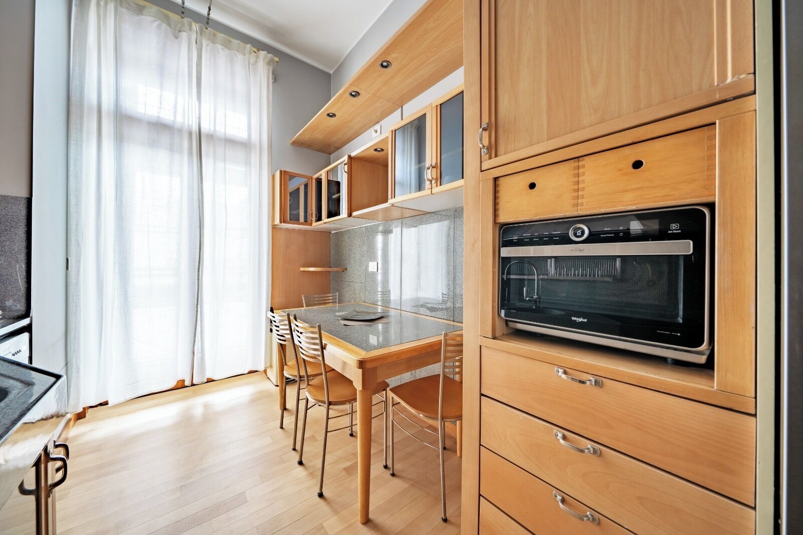 A modern kitchen with wooden cabinets, a built-in oven, and a dining area with chairs.