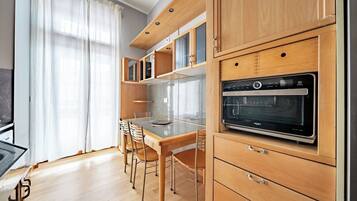 A modern kitchen with wooden cabinets, a built-in oven, and a dining area with chairs.