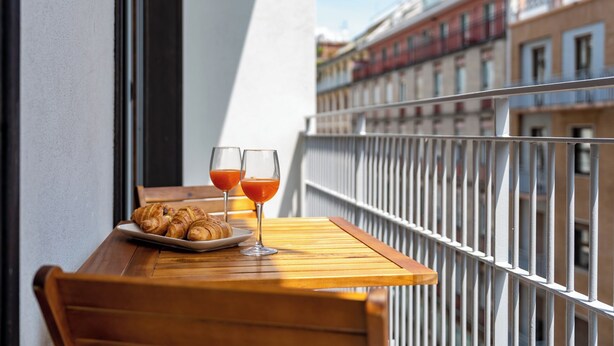 A balcony with a wooden table, two glasses of orange juice, and a plate of croissants. - Heart Milan Apartments Duomo Missori (Milan)