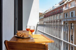 A balcony with a wooden table, two glasses of orange juice, and a plate of croissants.