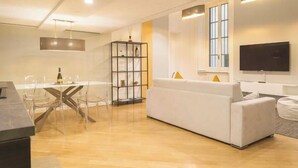 A modern living room with a white sofa, a dining table with chairs, a bookshelf, and a flat-screen TV mounted on the wall. - Heart Milan Apartments Duomo Missori (Milan)