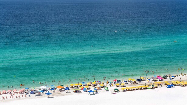 A beach with white sand, clear turquoise water, and numerous colorful umbrellas.