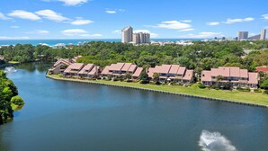 A riverside hotel with multiple buildings aligned along the water, featuring a calm river and lush greenery.