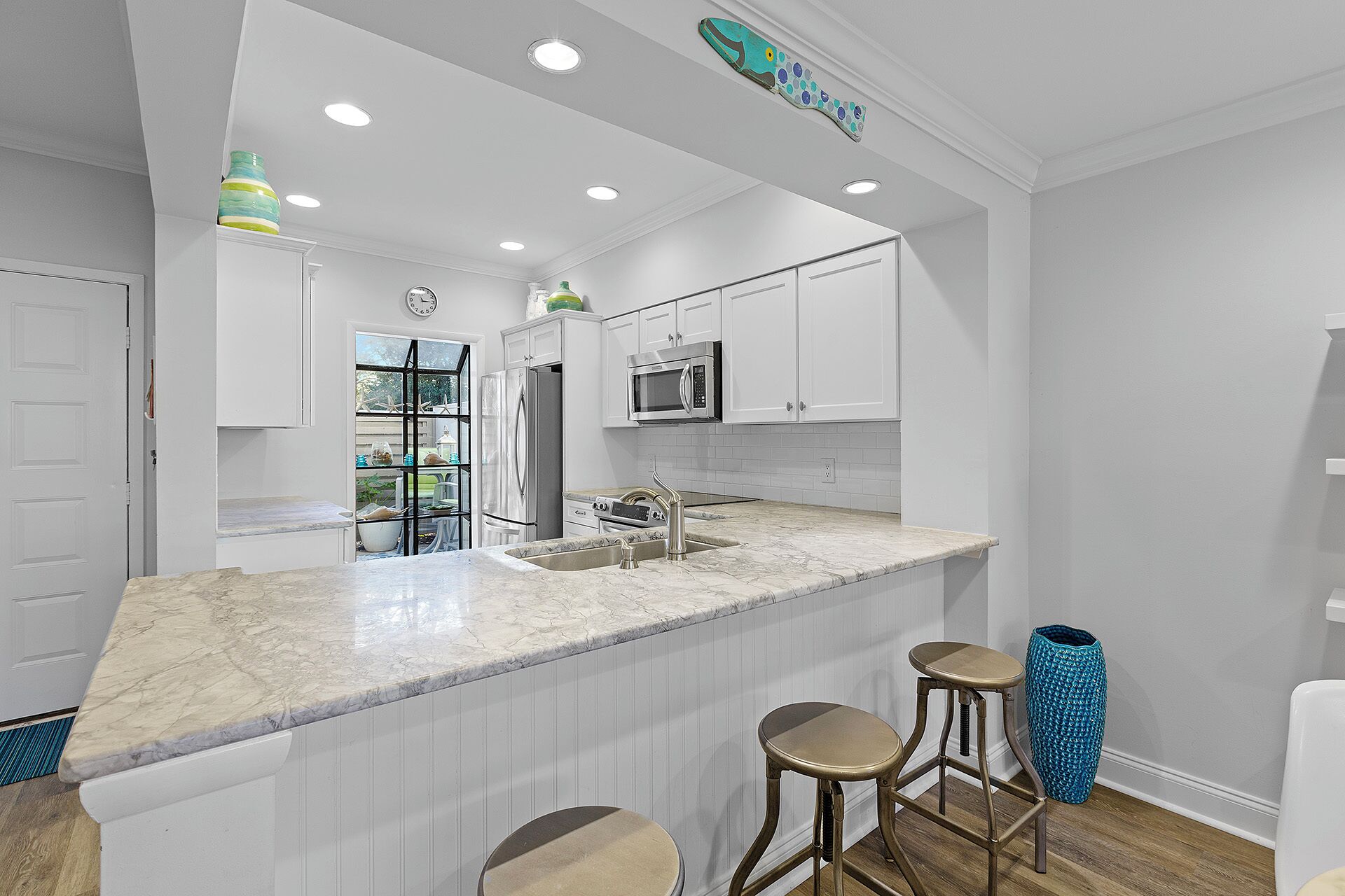 A modern kitchen with white cabinetry, a large island with bar stools, stainless steel appliances, and a decorative fish wall art piece.