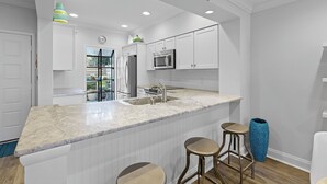 A modern kitchen with white cabinetry, a large island with bar stools, stainless steel appliances, and a decorative fish wall art piece.