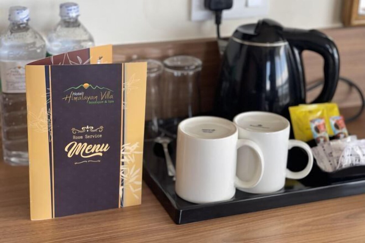 A hotel room service tray with a menu, two white mugs, a kettle, and bottled water.