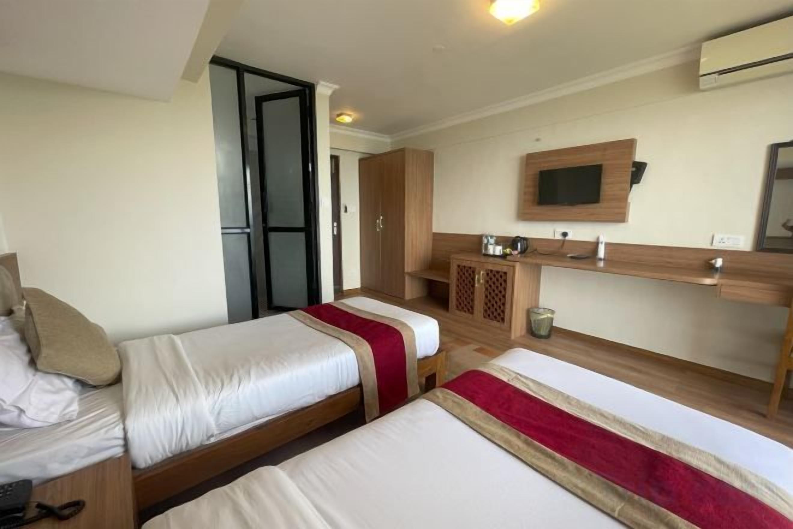 Una habitación de hotel con dos camas, una kitchenette pequeña, un televisor montado en la pared y una puerta corredera que da a otra habitación.