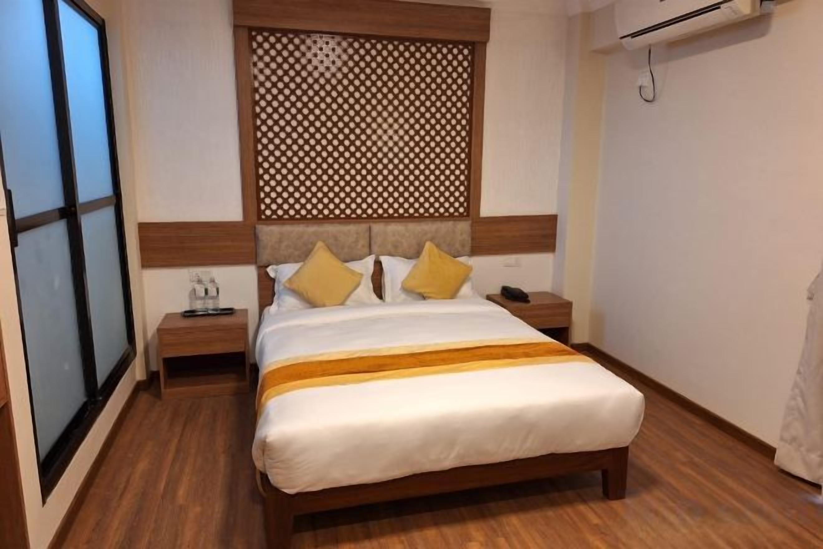 A hotel room with a bed, bedside tables, a decorative headboard, and a window.
