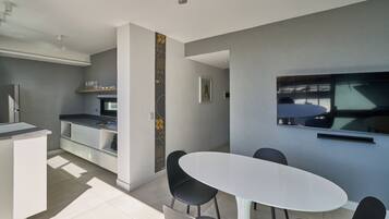 A modern kitchen with white cabinets, a built-in oven, and a dining area with a white table and black chairs.