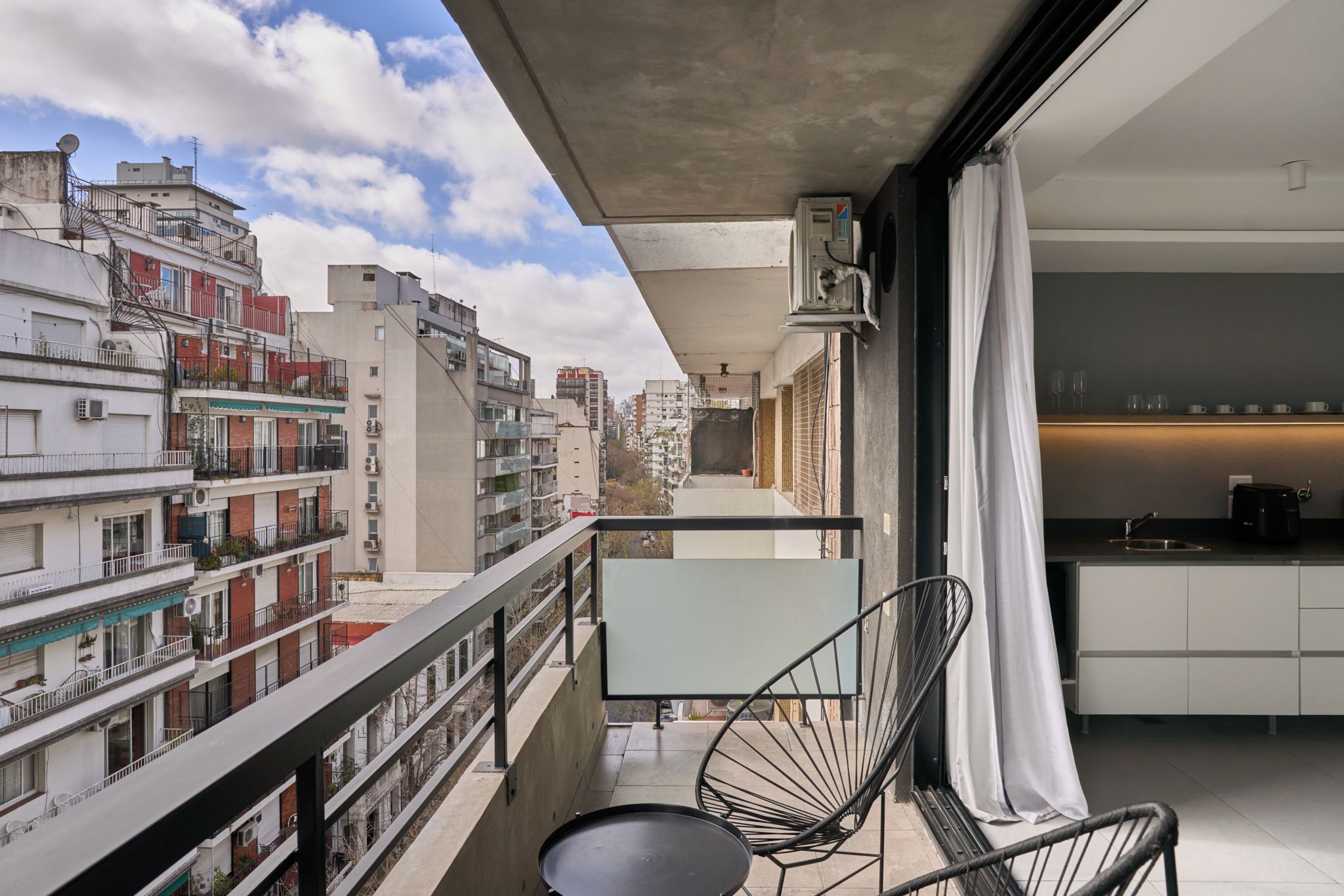 Un balcon offrant une vue sur le paysage urbain, un coin repas avec une table et des chaises, et une cuisine équipée d’appareils modernes.
