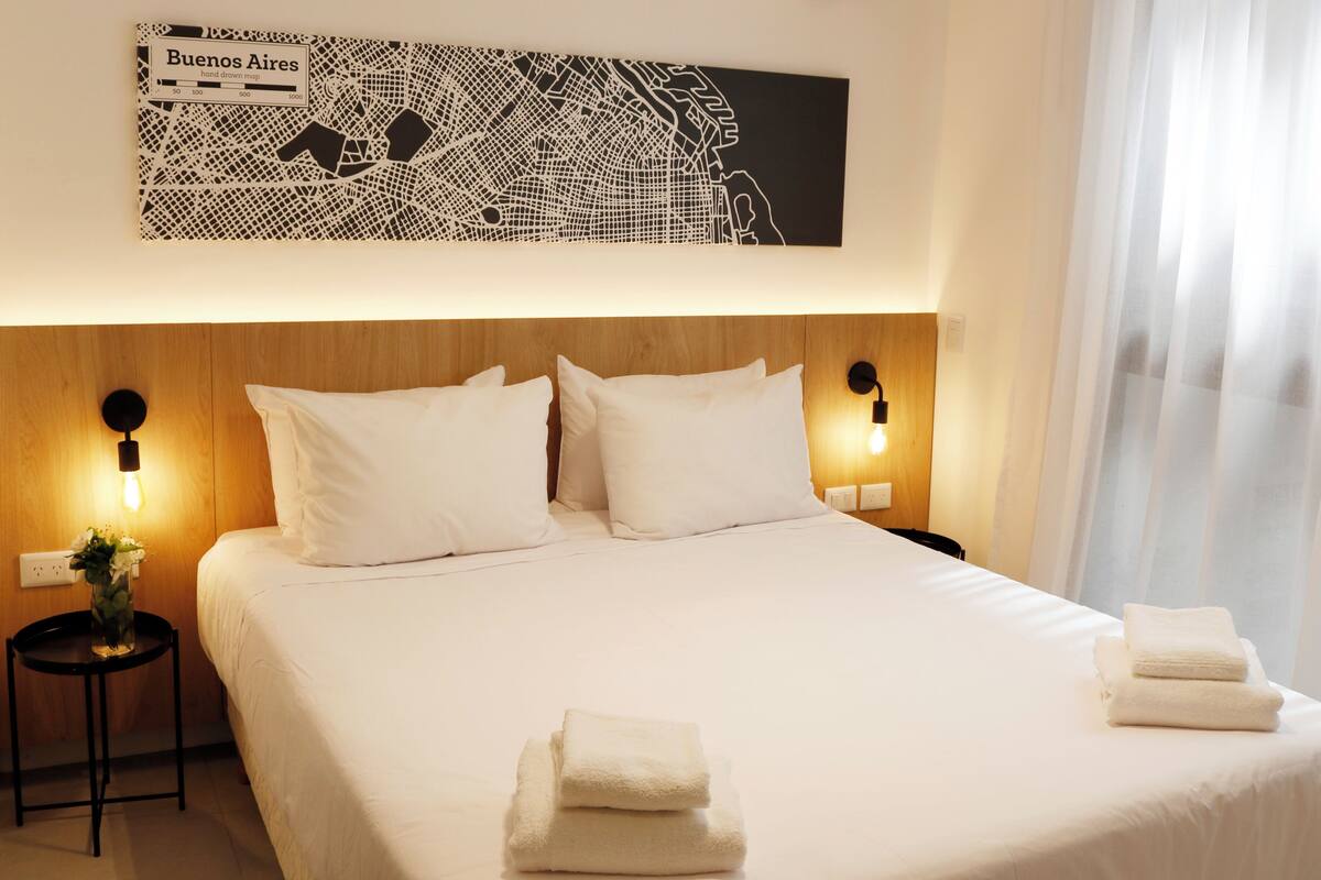 A hotel room with a large bed, two bedside tables, a wall map, and a window with curtains.