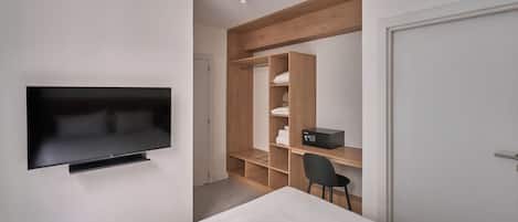 A modern bedroom with a flat-screen TV mounted on the wall, a wooden wardrobe, a desk with a chair, and a bed.