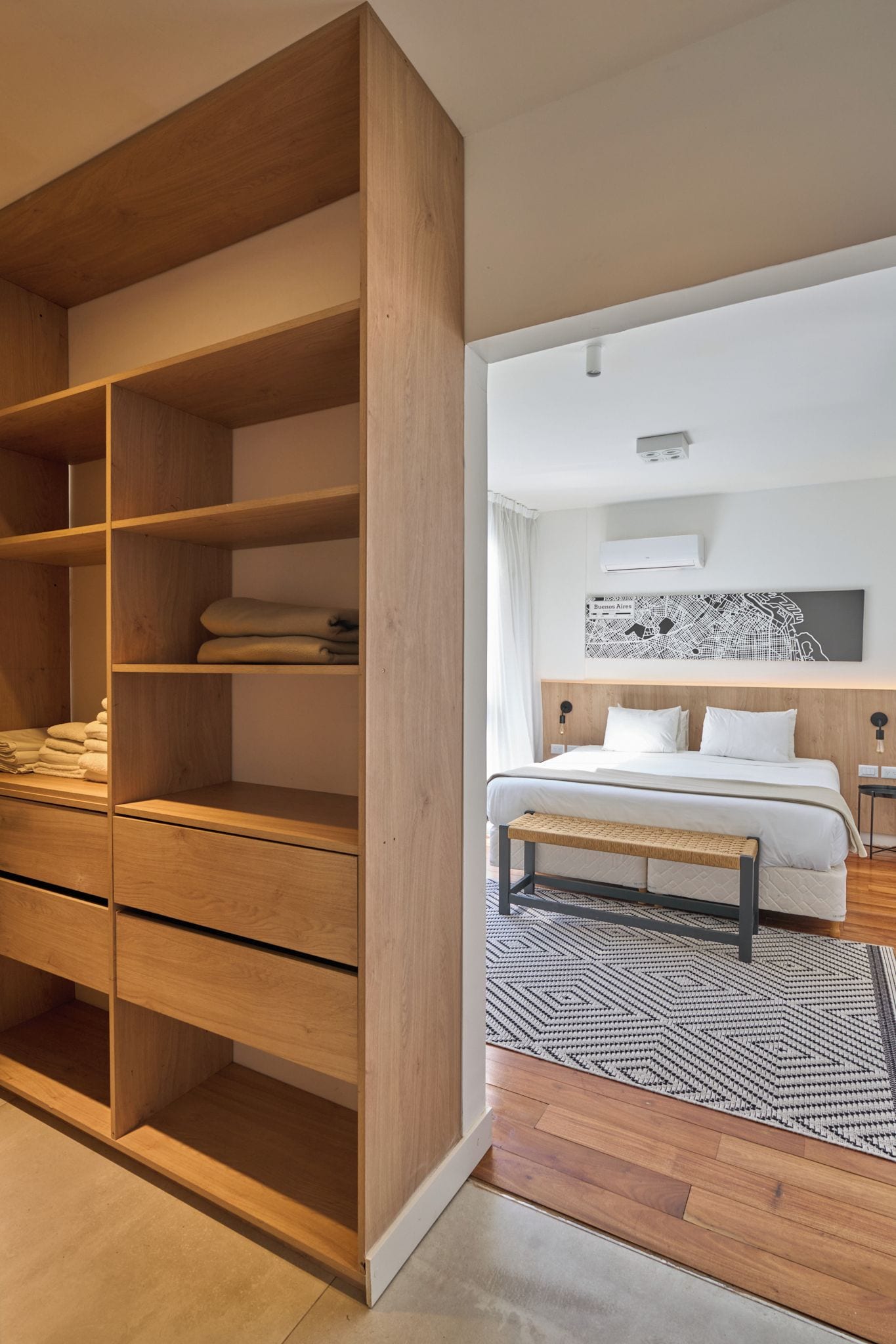 Une chambre à coucher moderne avec une armoire en bois, un lit doté d’une tête de lit et une carte accrochée au mur.