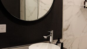 A bathroom with a round mirror, a white sink, and a black countertop. - Alma Rentals French Palermo (Buenos Aires)