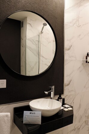 A bathroom with a round mirror, a white sink, and a black countertop. - Alma Rentals French Palermo (Buenos Aires)