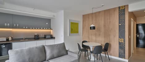 A modern living space with a grey sofa, a dining table with chairs, a kitchen area, and a wooden partition with a cityscape artwork.