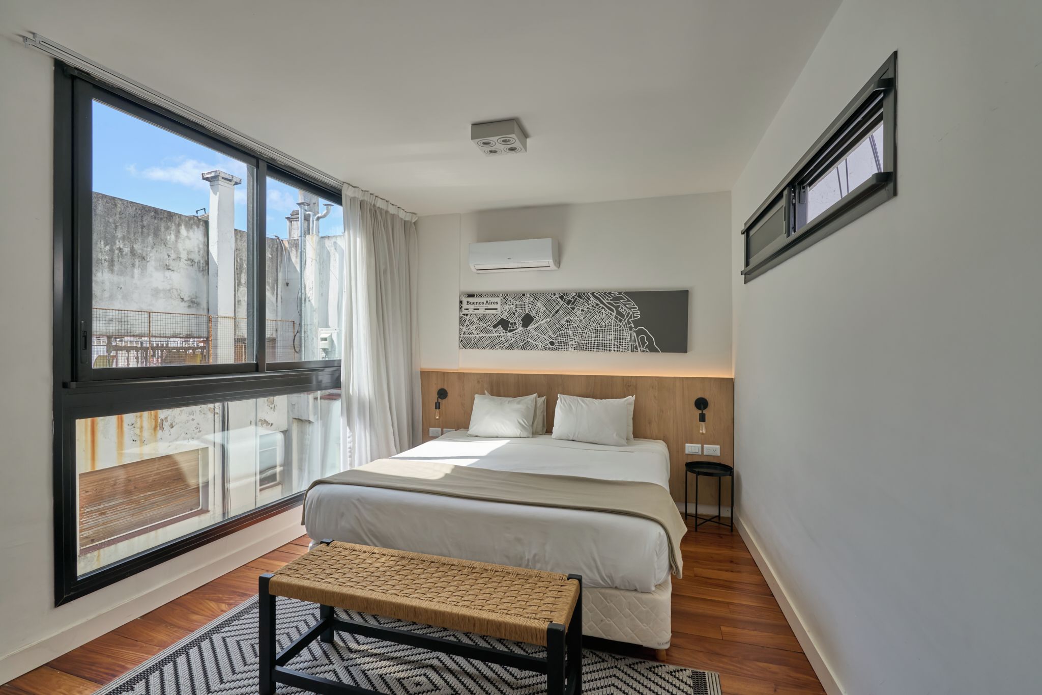 Une chambre à coucher moderne avec une grande fenêtre, un lit, un banc et une œuvre d’art représentant une carte accrochée au mur.