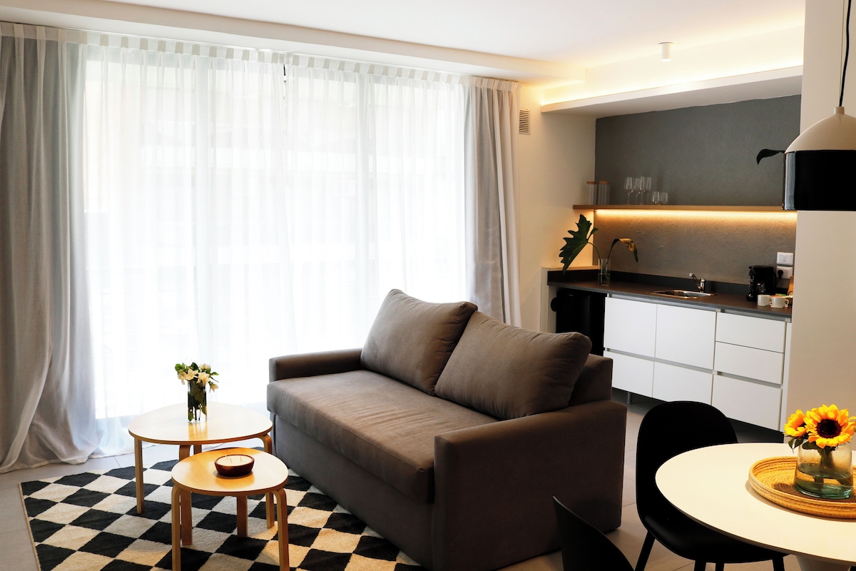 A modern living room with a sofa, a small table with a vase of flowers, and a checkered rug.