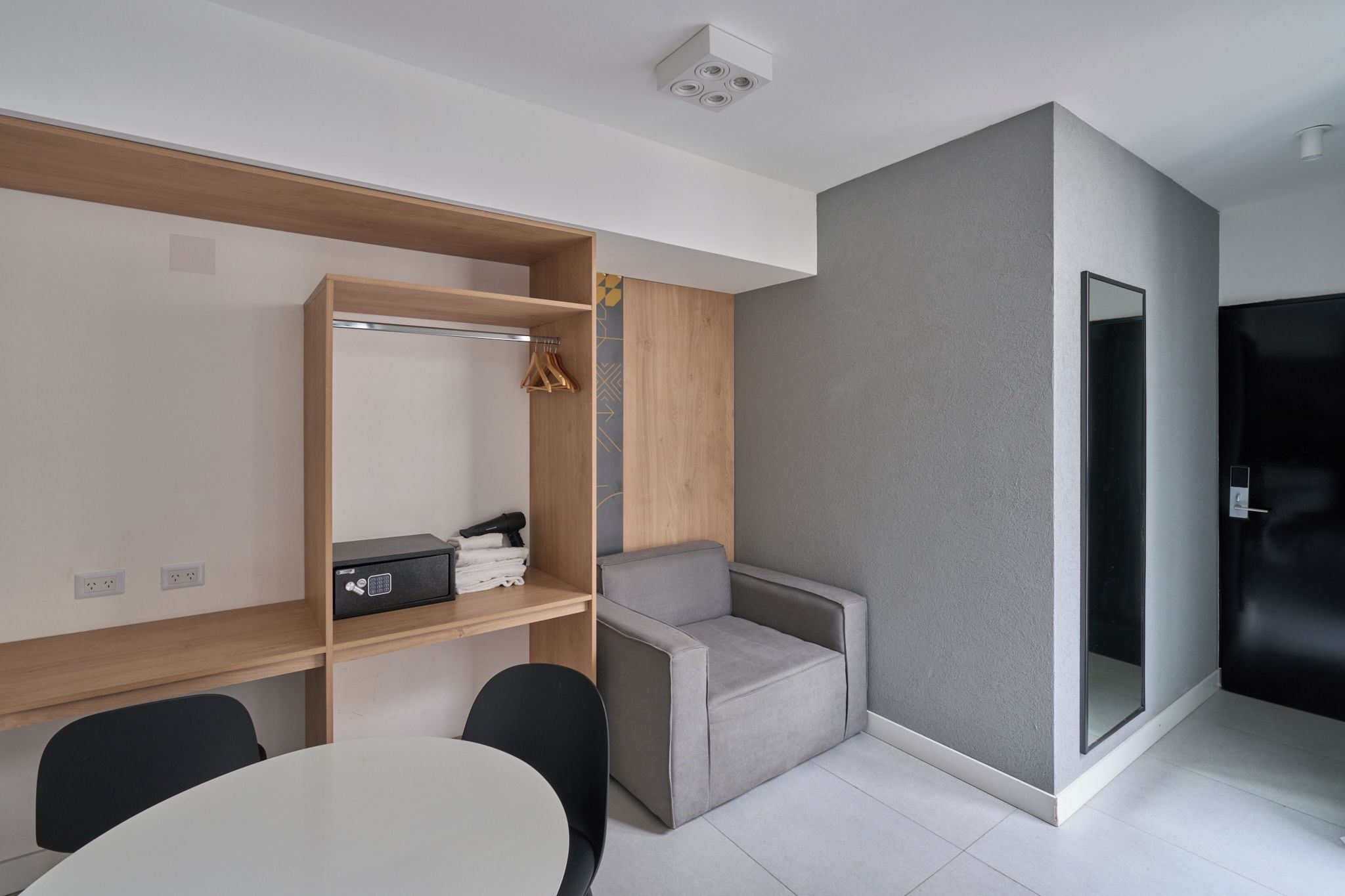 Quarto moderno com mesa branca, sofá cinza, estantes de madeira e parede cinza de destaque.