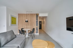 A modern living room with a grey sofa, a round wooden coffee table, and a dining area with a white table and black chairs. - Alma Rentals French Palermo (Buenos Aires)