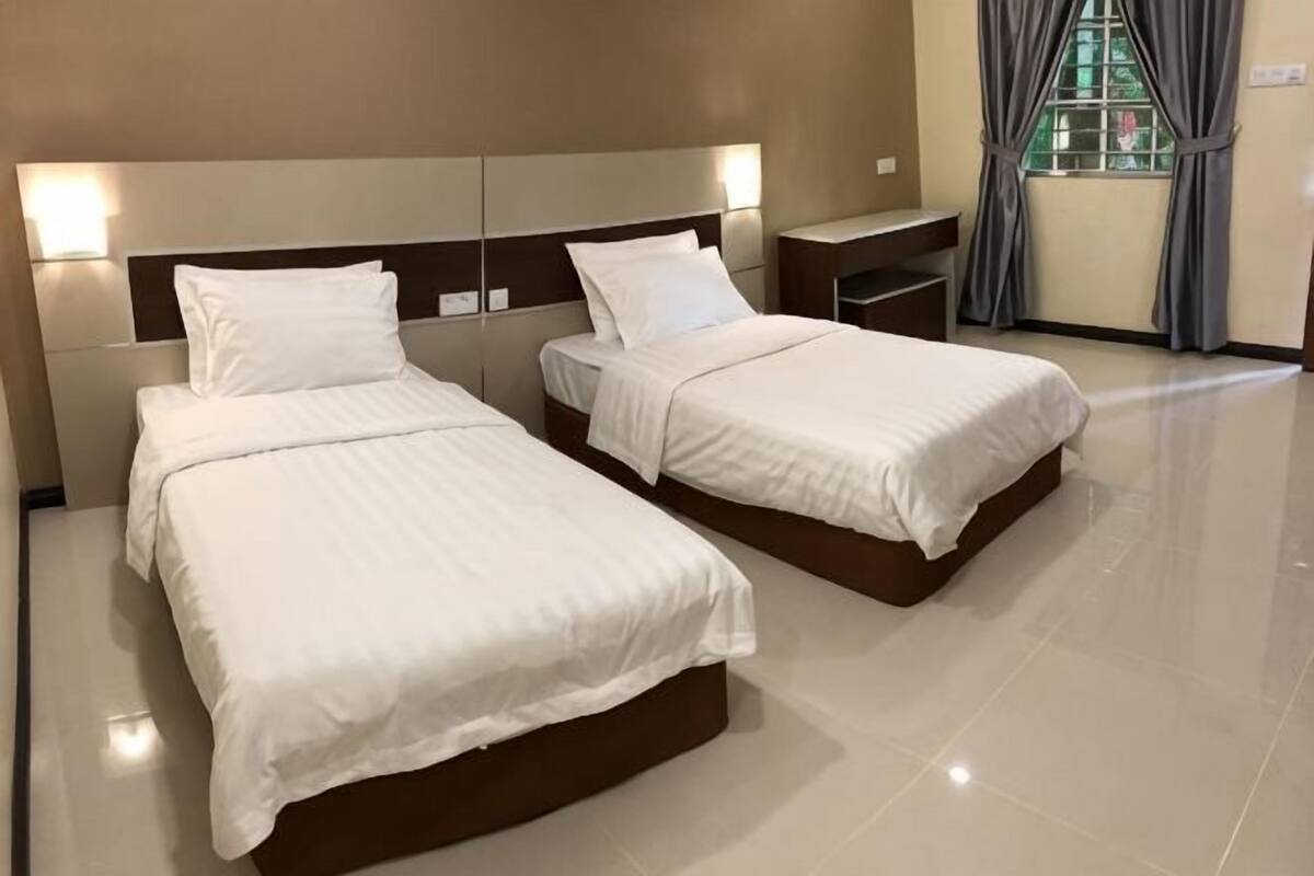 A hotel room with two beds, a nightstand, and a window with curtains.