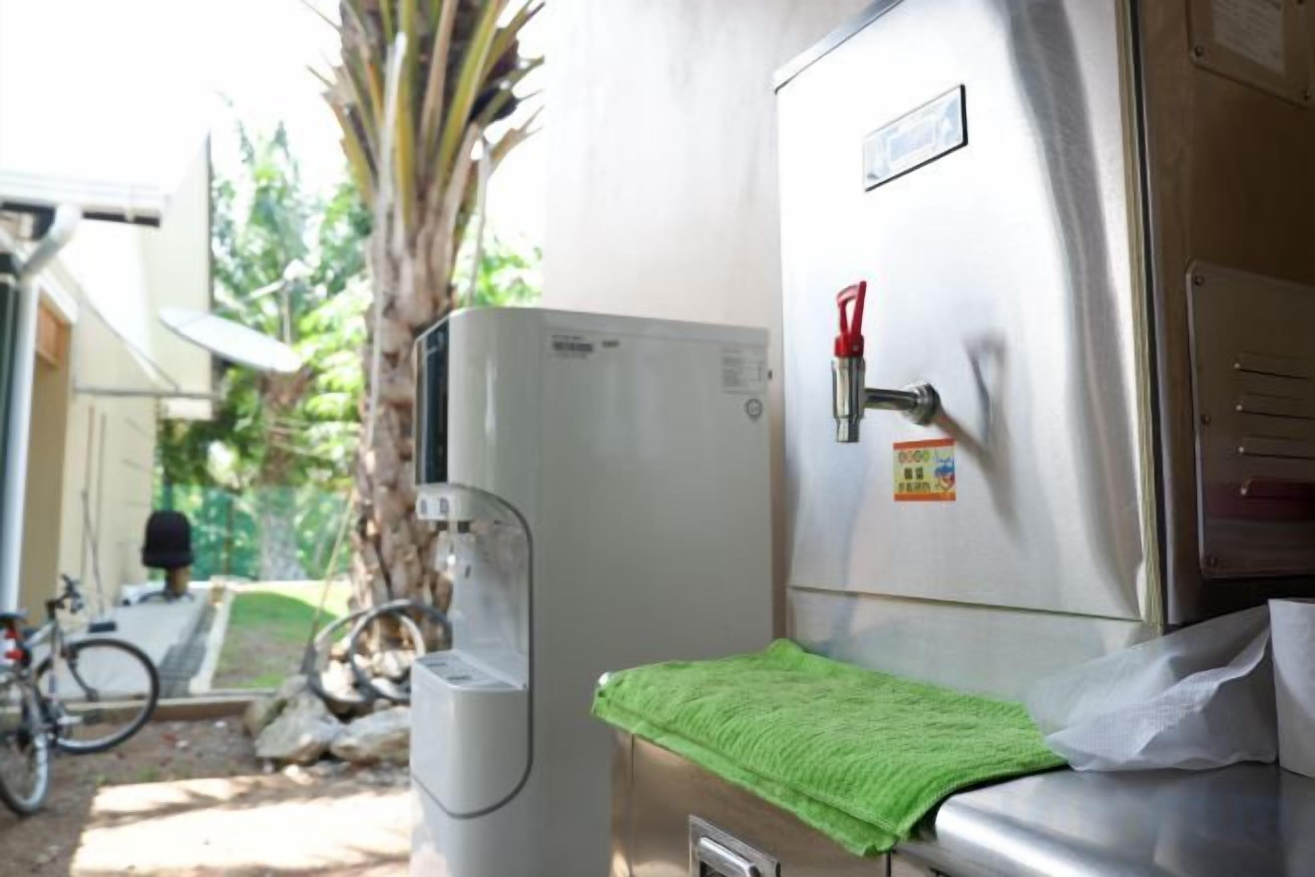 A compact refrigerator with a water dispenser, a green towel on the counter, and a fire extinguisher mounted on the wall.