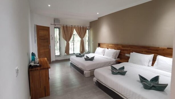 A hotel room with two beds, a wooden headboard, a small desk, and a window with curtains. - Hemingway Cottage (Semporna)
