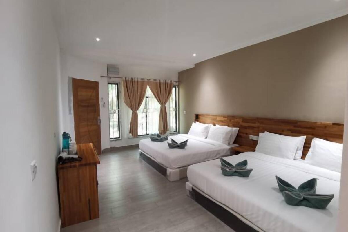 A hotel room with two beds, a wooden headboard, a small desk, and a window with curtains.