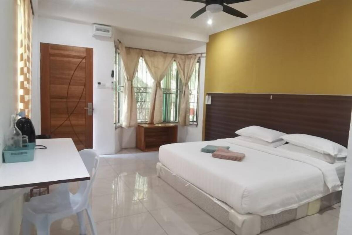 A bedroom with a bed, a desk, a chair, a window with curtains, and a ceiling fan.