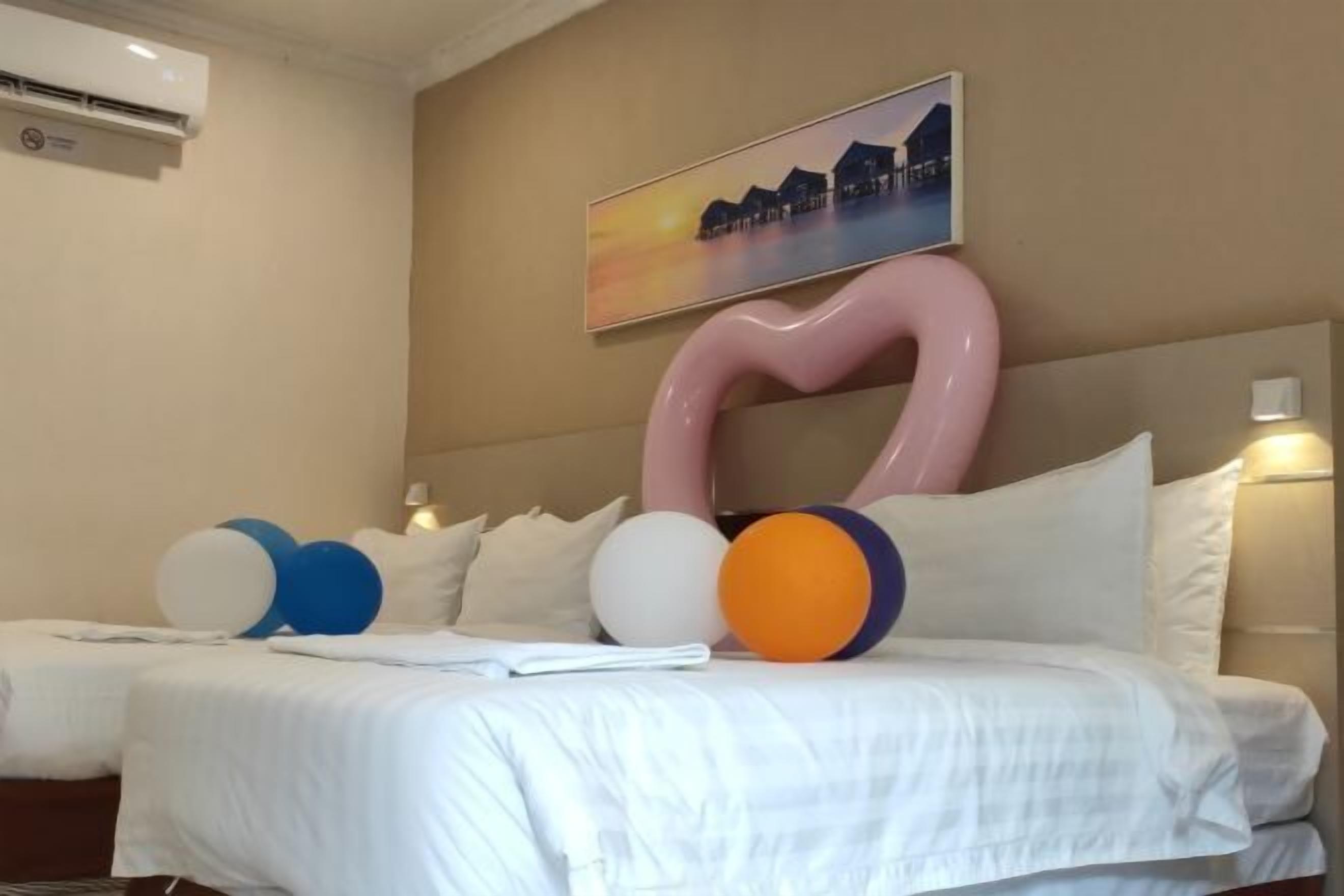 A hotel room with a bed, pillows, and a large abstract art piece on the wall.