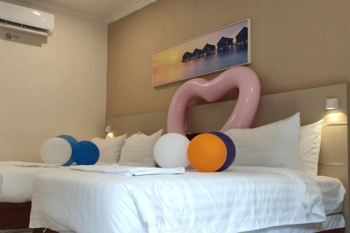 Ett hotellrum med en säng, kuddar och ett stort, abstrakt konstverk på väggen.