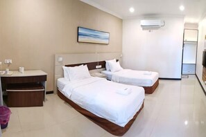 A hotel room with two beds, a desk, a chair, a trash bin, and a painting on the wall. - Hemingway Cottage (Semporna)