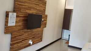 A room with a wooden wall panel, a mounted television, and a white switchboard. - Hemingway Cottage (Semporna)