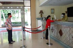 A reception area with a counter, a red rope barrier, and a person standing at the counter. - Puri Asri Hotel & Resort Magelang (Central Magelang)