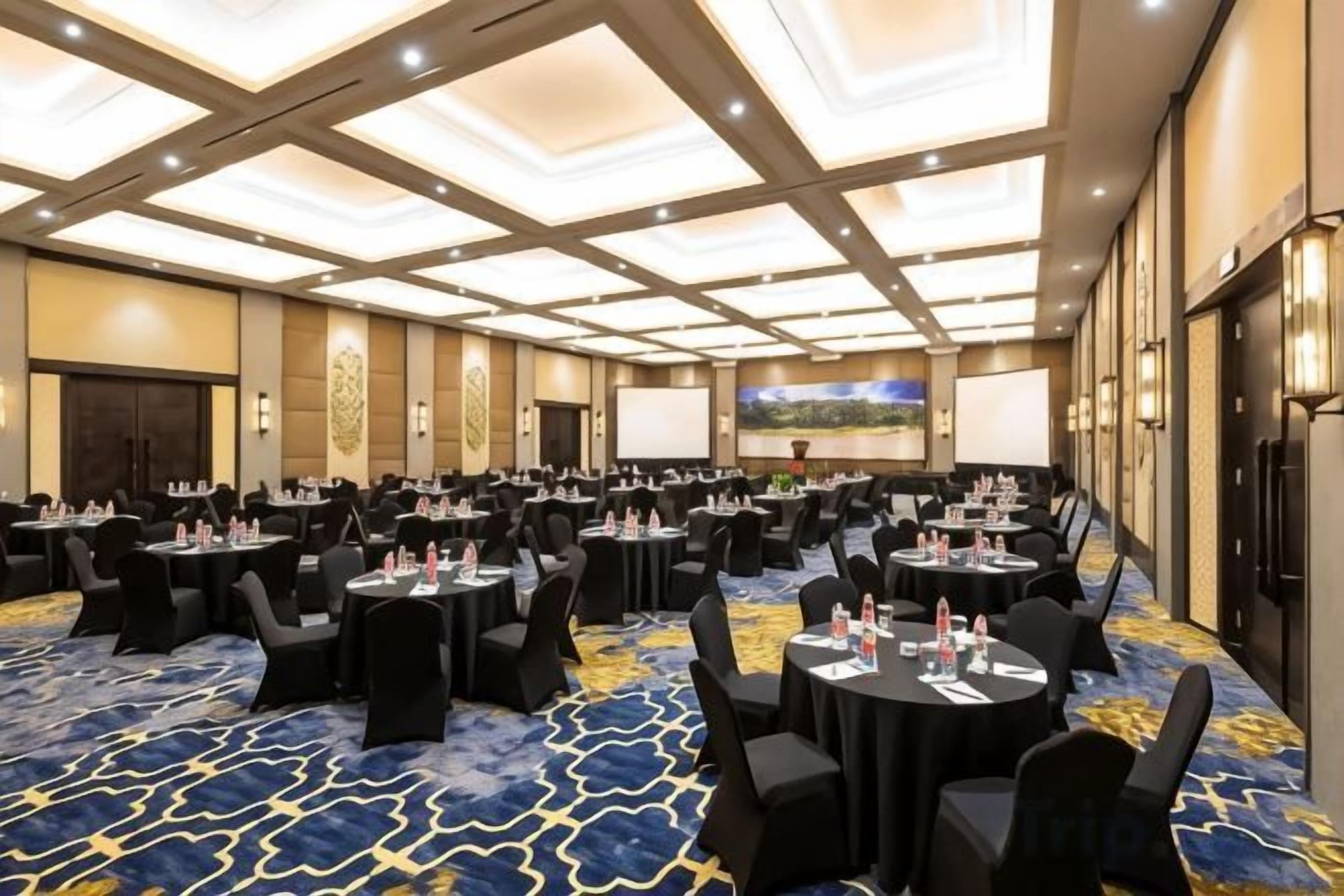 Un salón de conferencias con varias mesas y sillas, una pantalla grande y piso alfombrado.