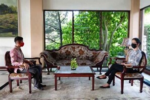 A room with a large window, a sofa, a coffee table, and two chairs. - Puri Asri Hotel & Resort Magelang (Central Magelang)