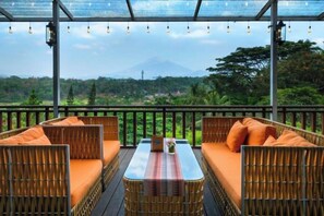 An outdoor seating area with wicker furniture and a table, overlooking a mountainous landscape. - Puri Asri Hotel & Resort Magelang (Central Magelang)