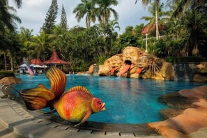 A swimming pool with a tropical setting, including palm trees and a rock formation with faces. - Puri Asri Hotel & Resort Magelang (Central Magelang)