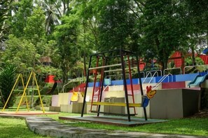Un terrain de jeux avec des balançoires et des toboggans, entouré d’arbres.